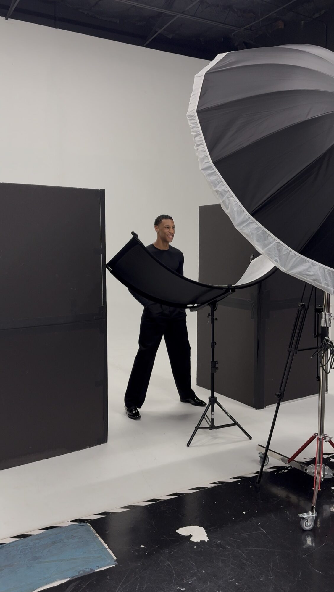 Person standing in a photography studio with large black and white equipment, black walls, and a white floor.