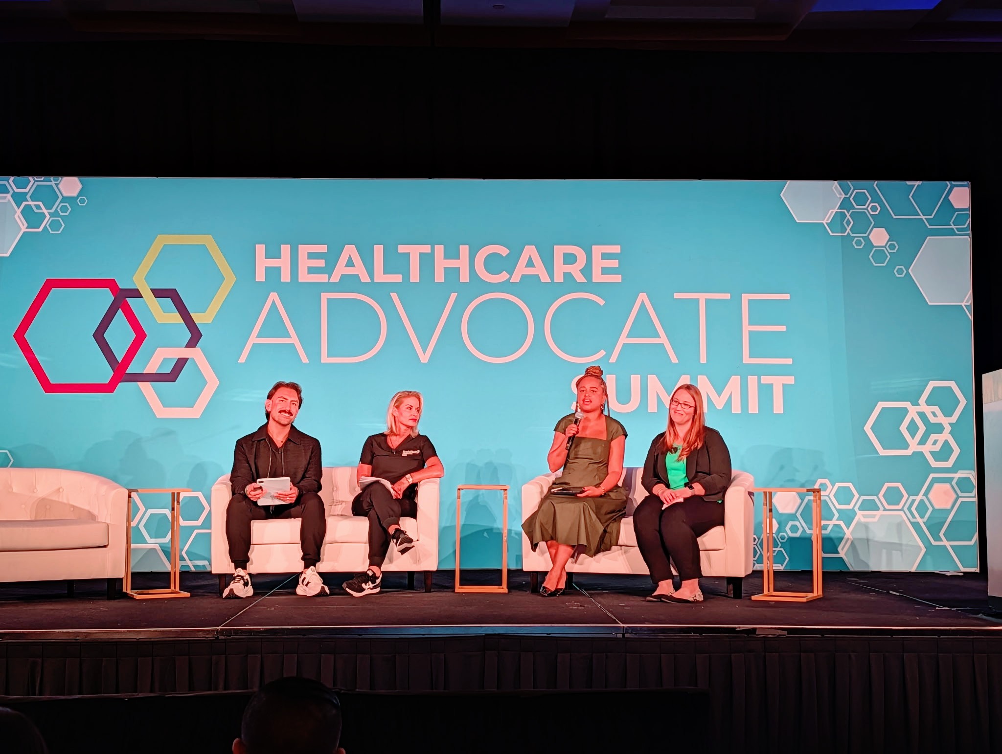 Four people sit on stage chairs in front of a blue background with healthcare advocacy summit text.