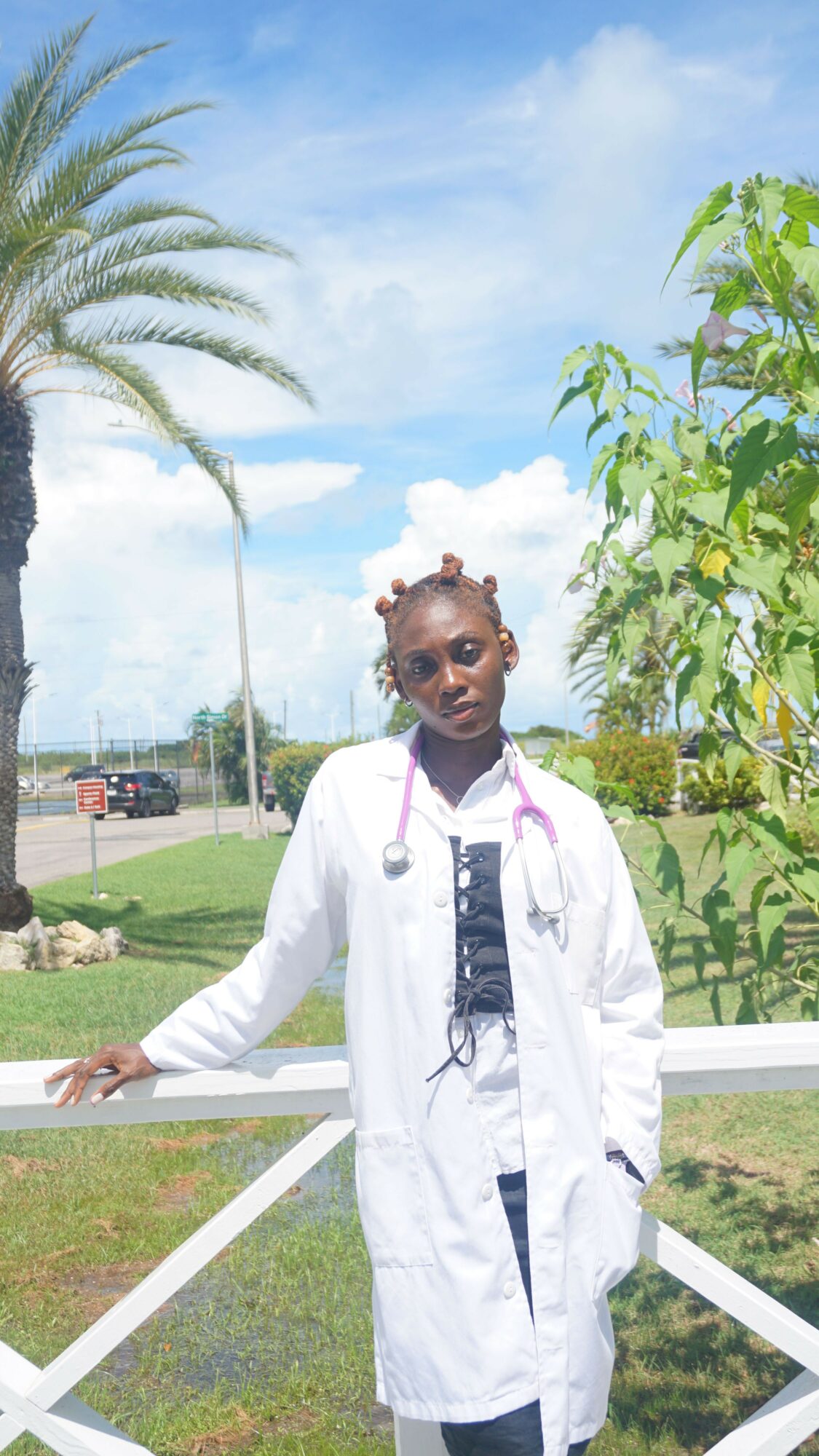 Woman in white coat standing outdoors with palm trees and blue sky in background.