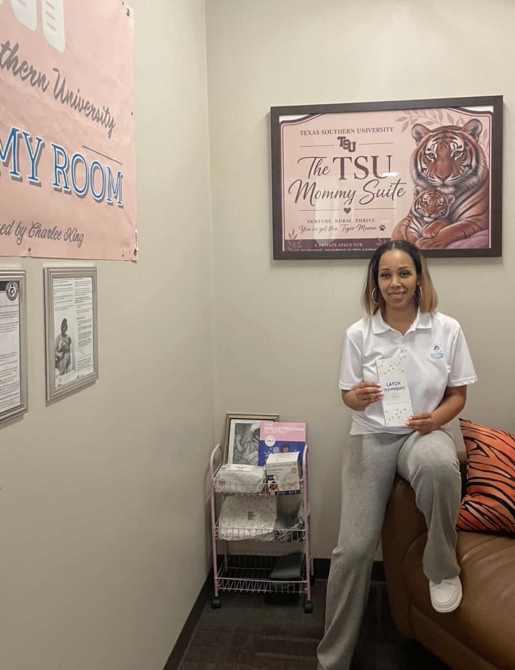 Young woman sitting on a couch holding a paper, in a room with framed artwork and posters on the wall.