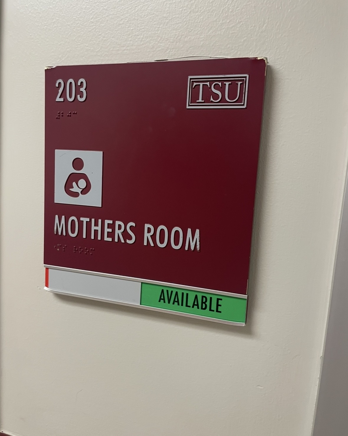 Maroon sign on wall indicating room 203, TSU, mothers room, available, with white and green sections.