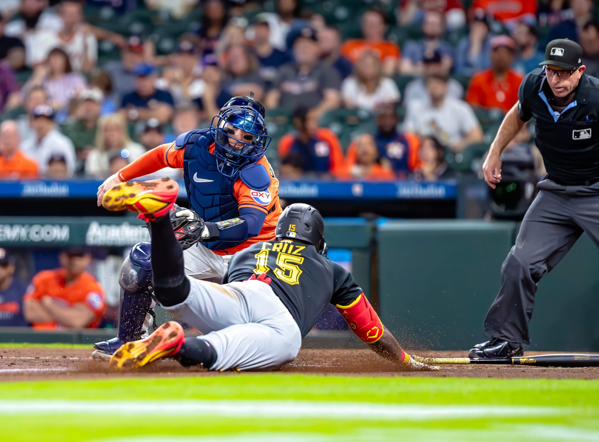 Baseball player sliding into home plate with catcher and umpire nearby, crowd in background