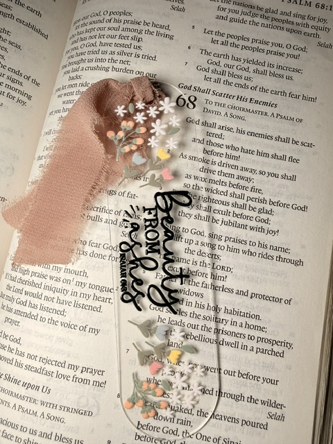 A handwritten note on a newspaper background with floral decorations and a pink paint stroke, reading 'Beauty from ashes'.