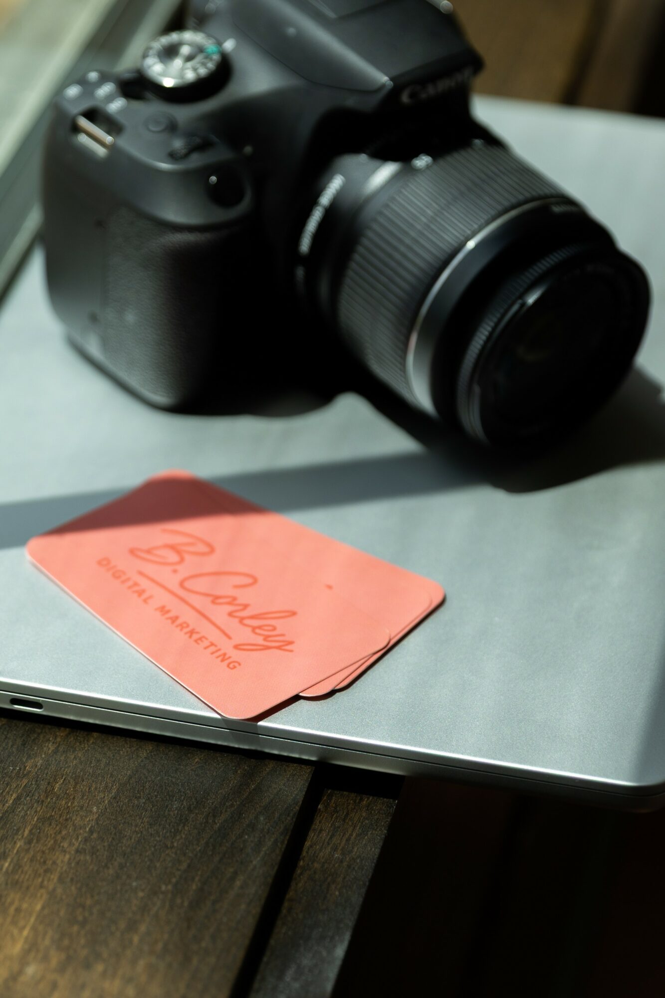 Camera with a large lens placed on a laptop, with a red card nearby on a table.