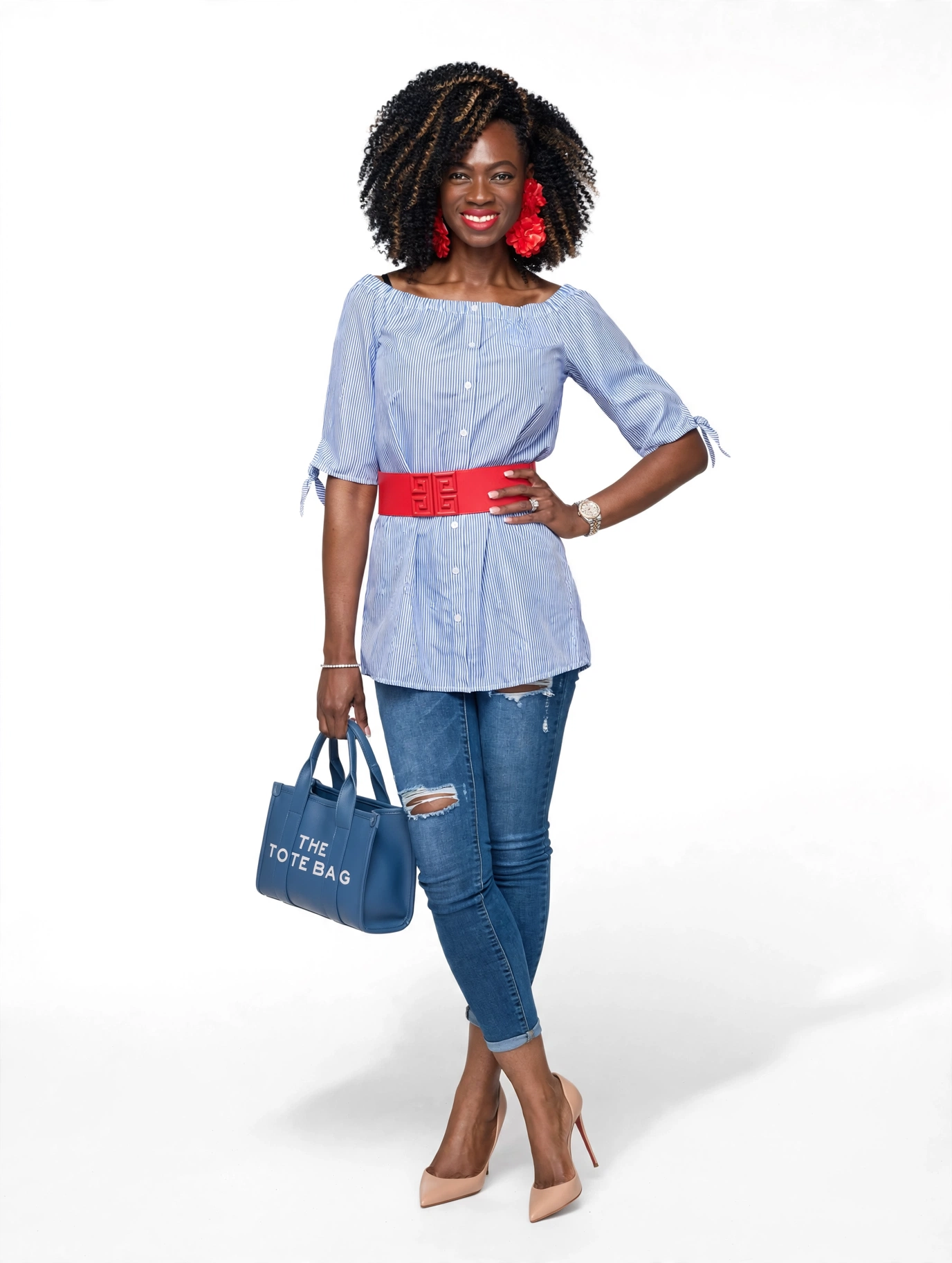Woman with curly hair wearing a blue striped top, red belt, jeans, beige heels, holding a blue bag, smiling.