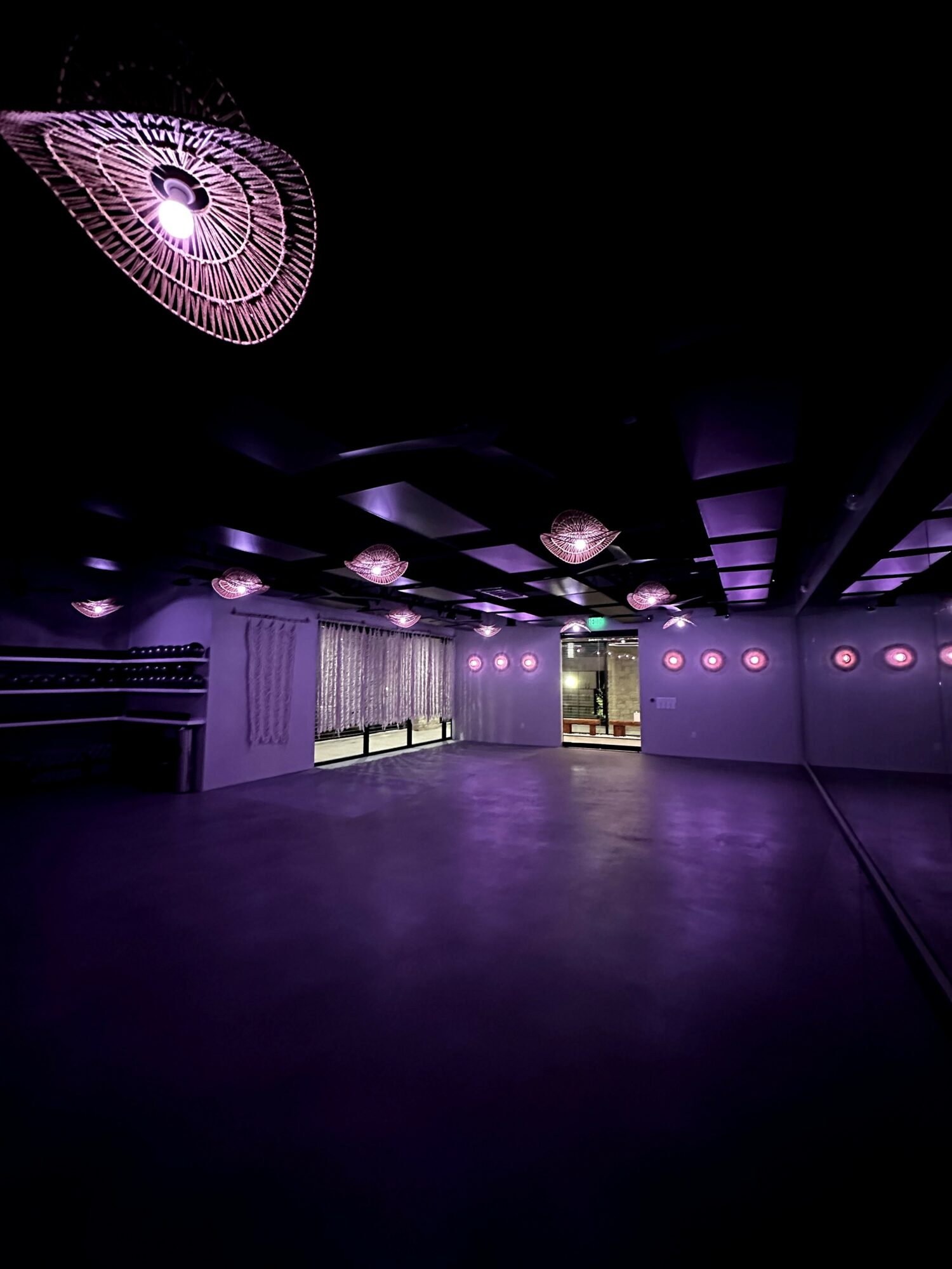 Empty dance or event space with purple lighting and decorative ceiling lights, large windows, and a dark floor.