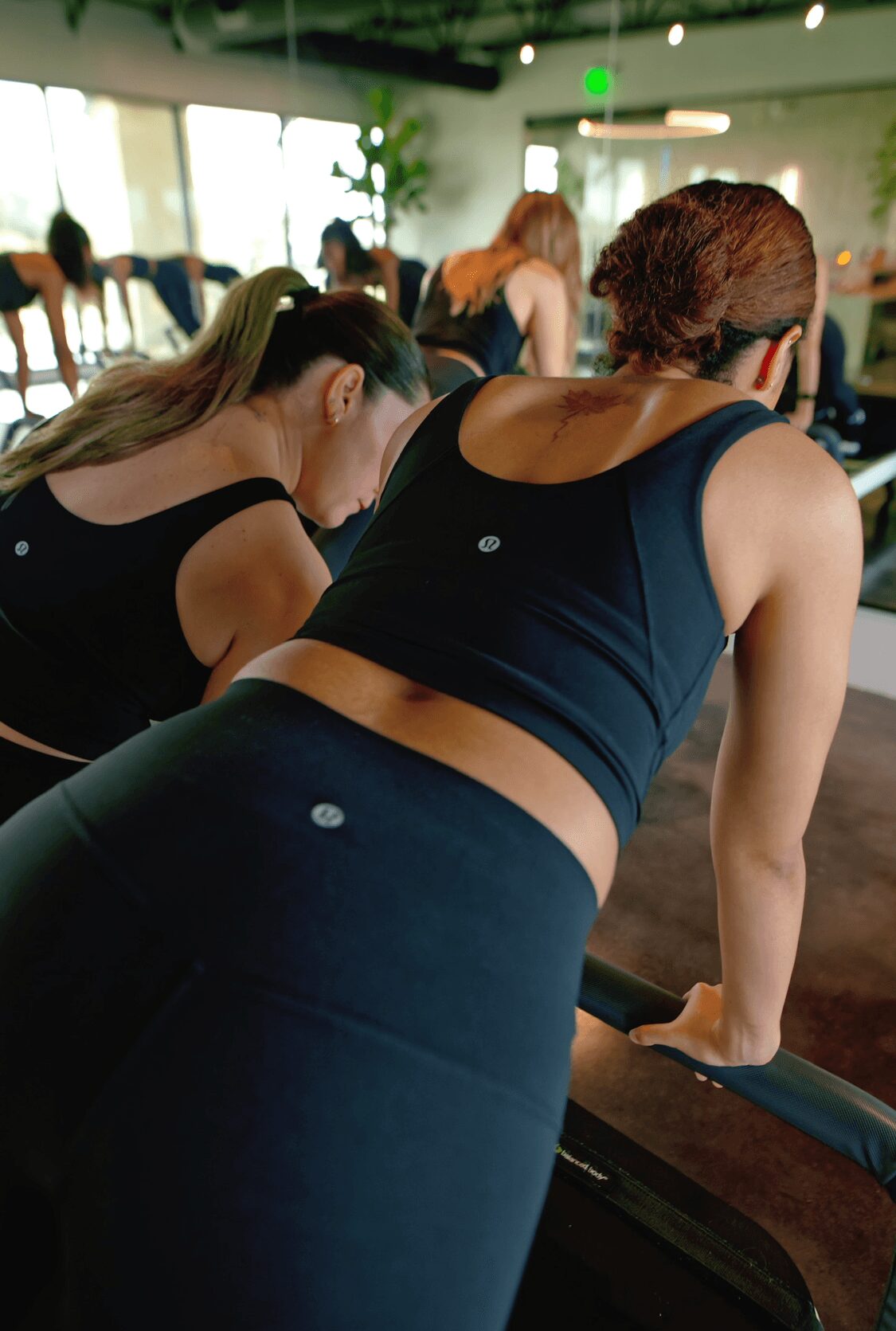 People exercising in a gym, focusing on a woman in a black sports bra and leggings leaning on a workout machine.