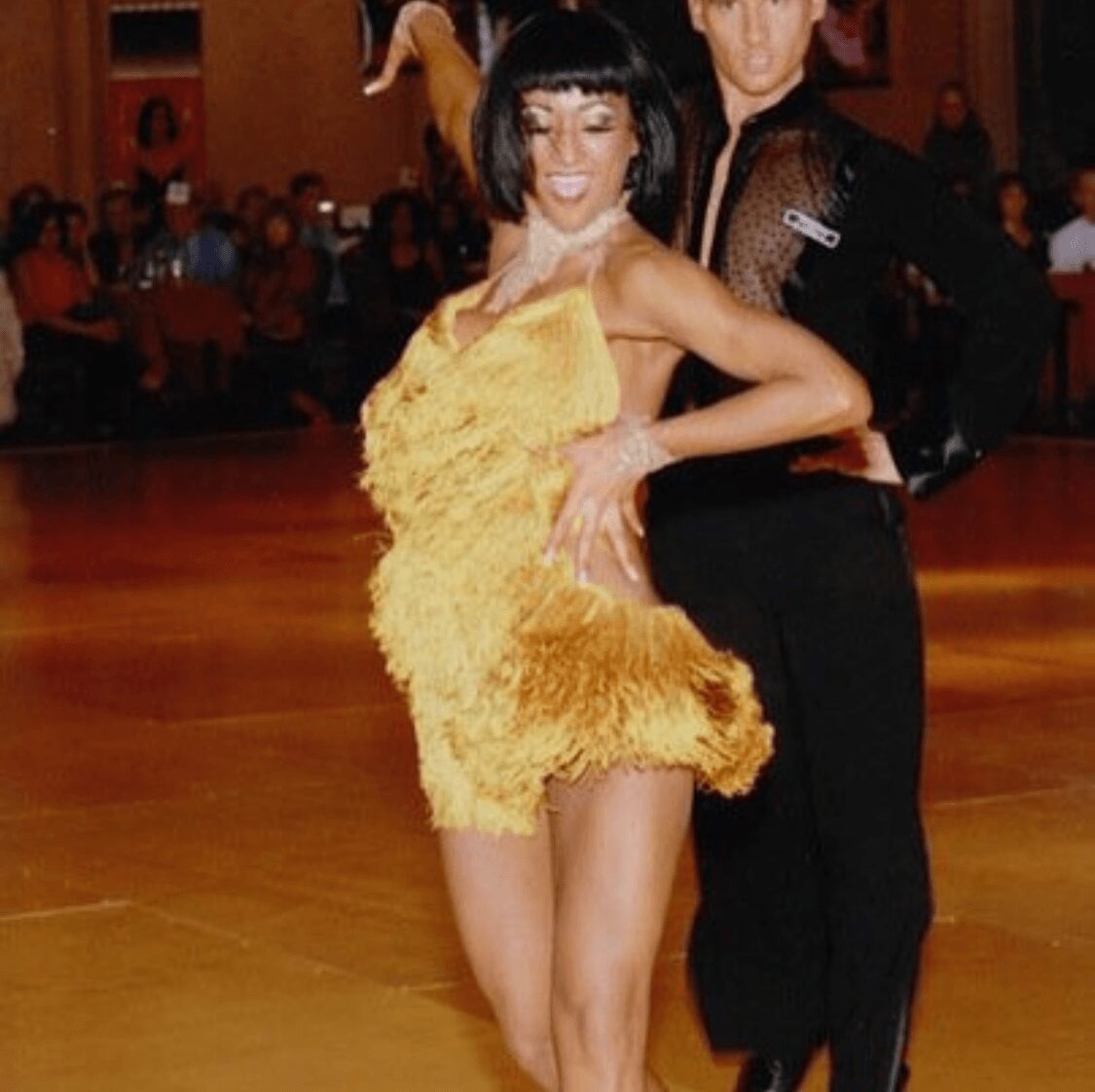 A woman in a yellow dress dancing with a man in black attire on a dance floor.