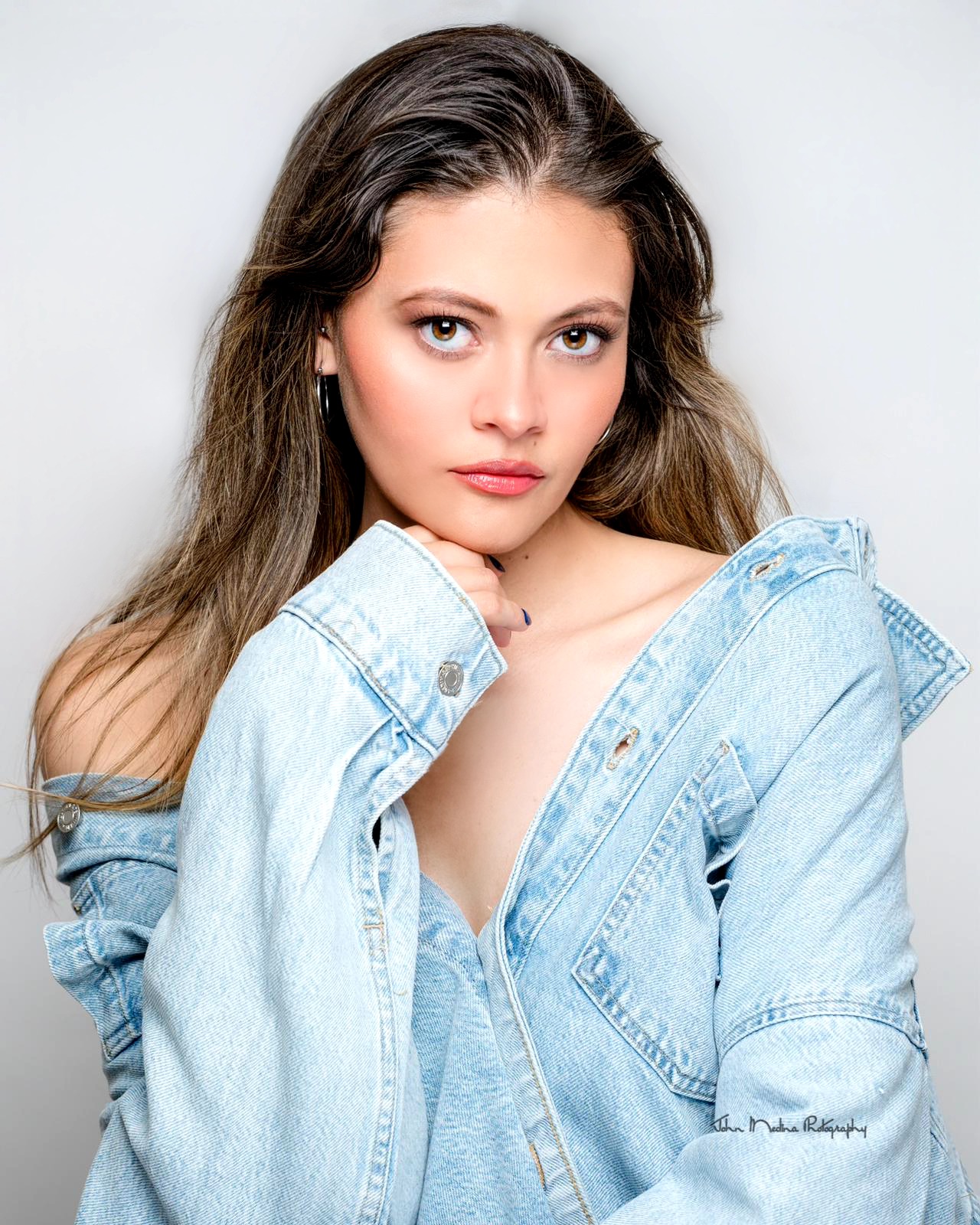 Young woman with long brown hair wearing a light blue denim jacket, looking at the camera with a neutral expression.