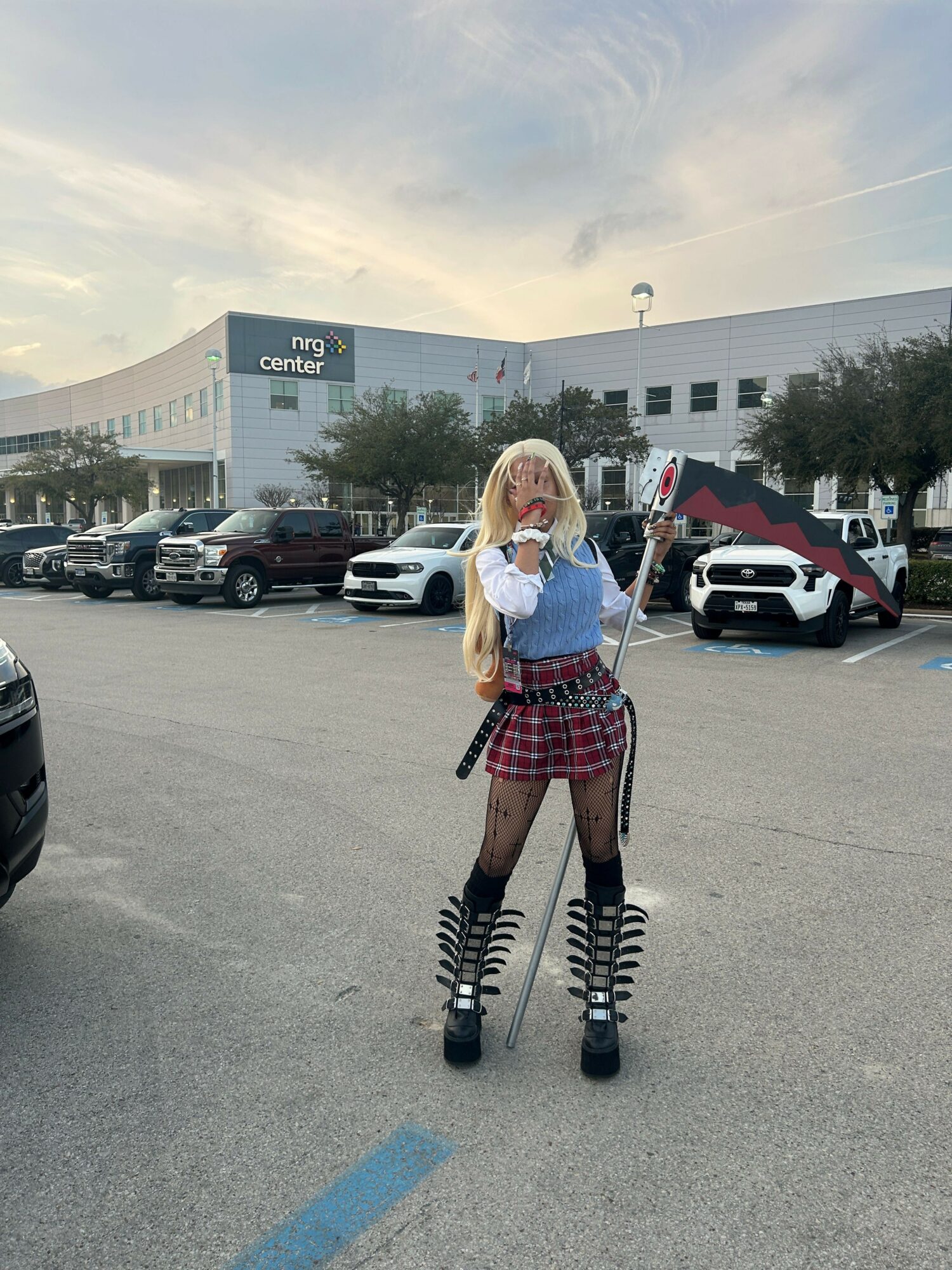 Person in school uniform standing in parking lot with cars and a building in background.