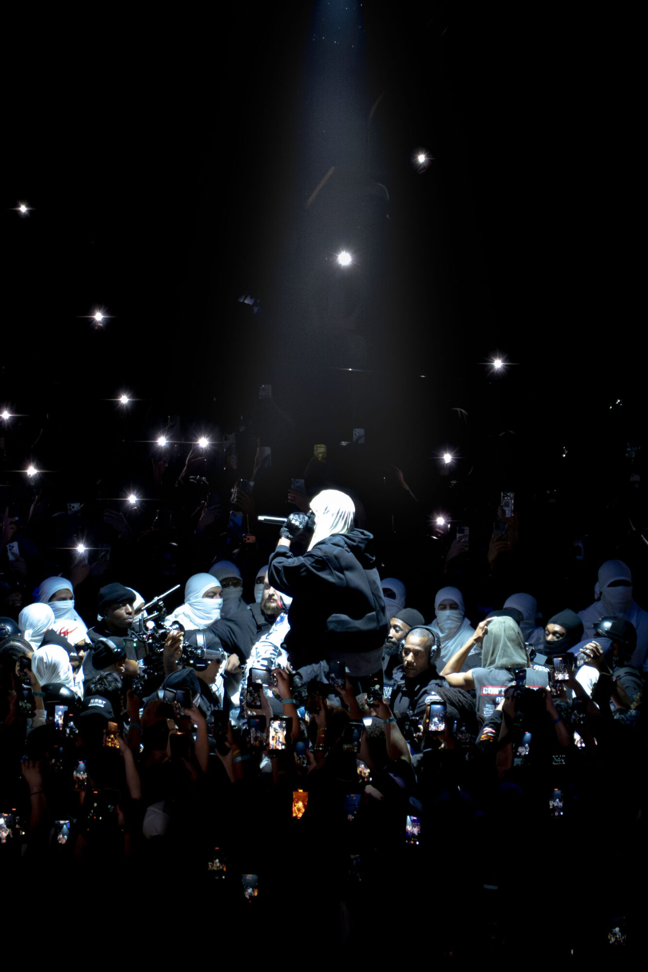 Performer on stage with a spotlight, surrounded by an audience, in a dark setting with star-like lights.