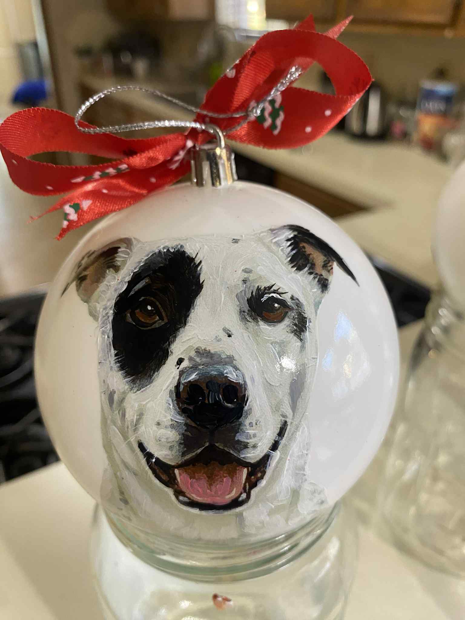 Dog's face painted on a Christmas ornament with a red ribbon bow on top.