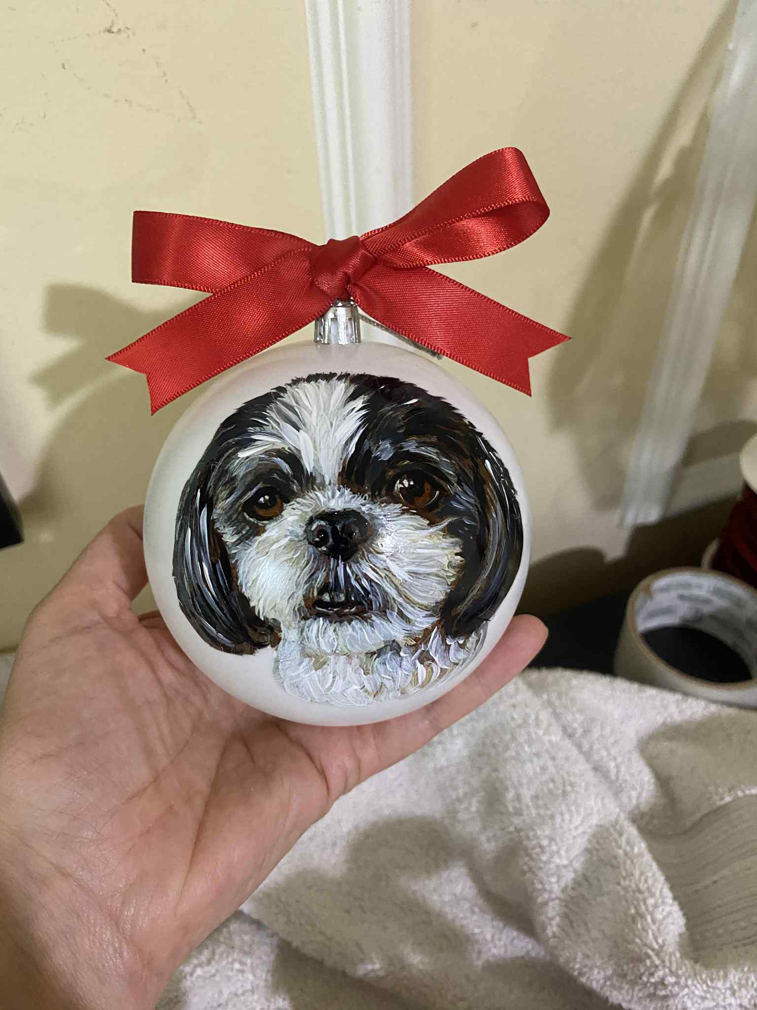 Hand holding a round ornament with a dog's face, decorated with a red ribbon bow on top.