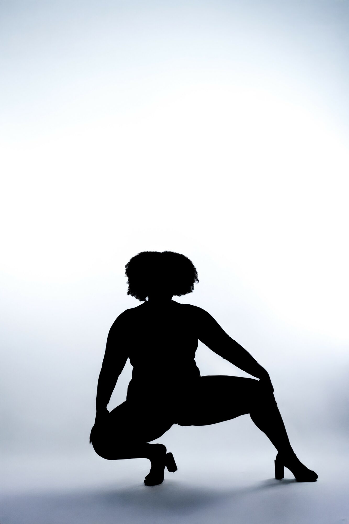 Silhouette of a person crouching with one knee raised, against a bright background.