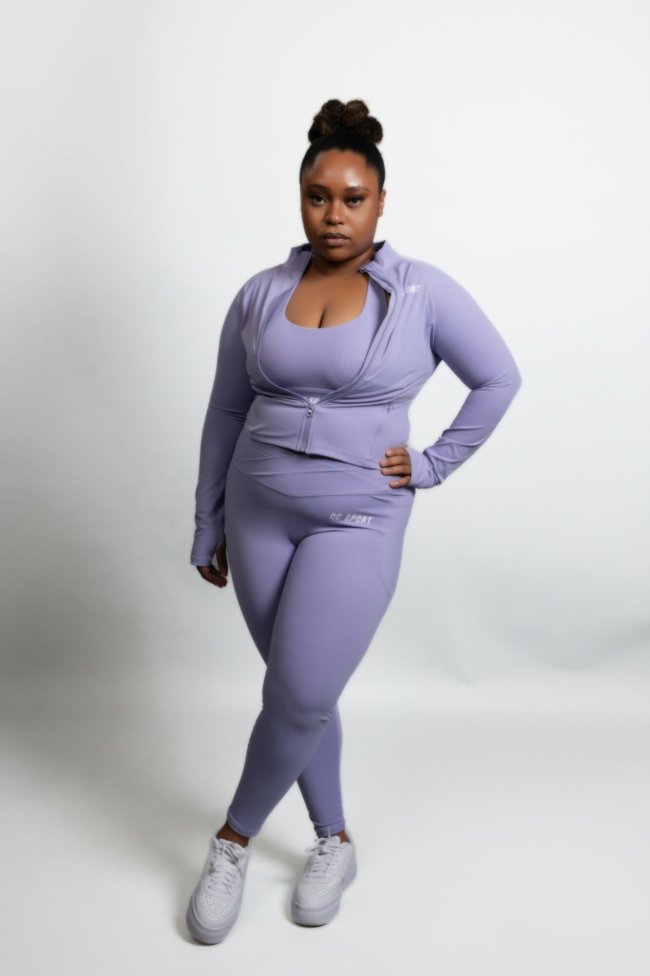 Woman in lavender athletic outfit standing with hand on hip, facing camera, against plain white background.