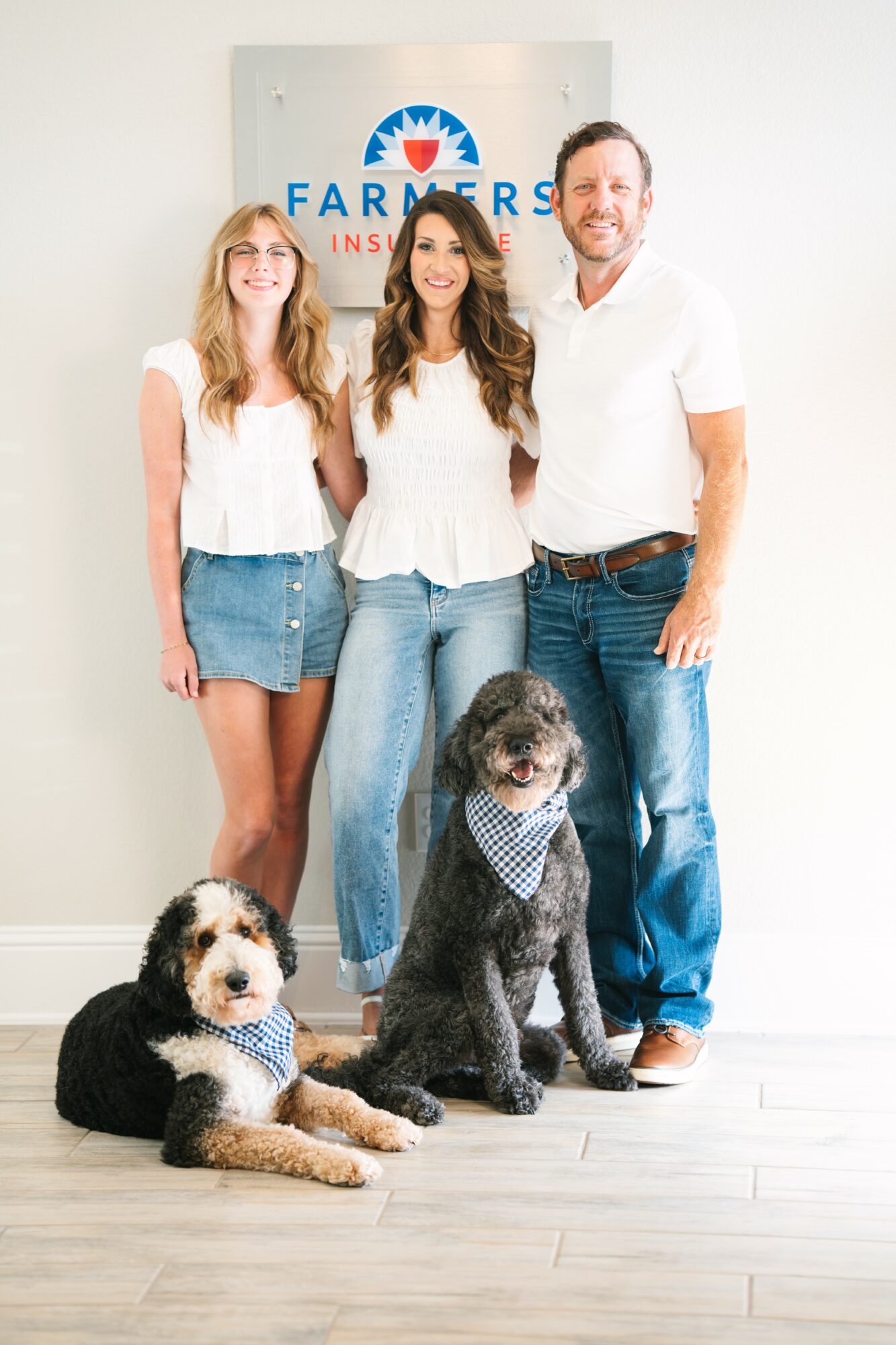 Three people and two dogs standing in front of a Farmers Insurance sign, smiling, with dogs sitting on the floor.