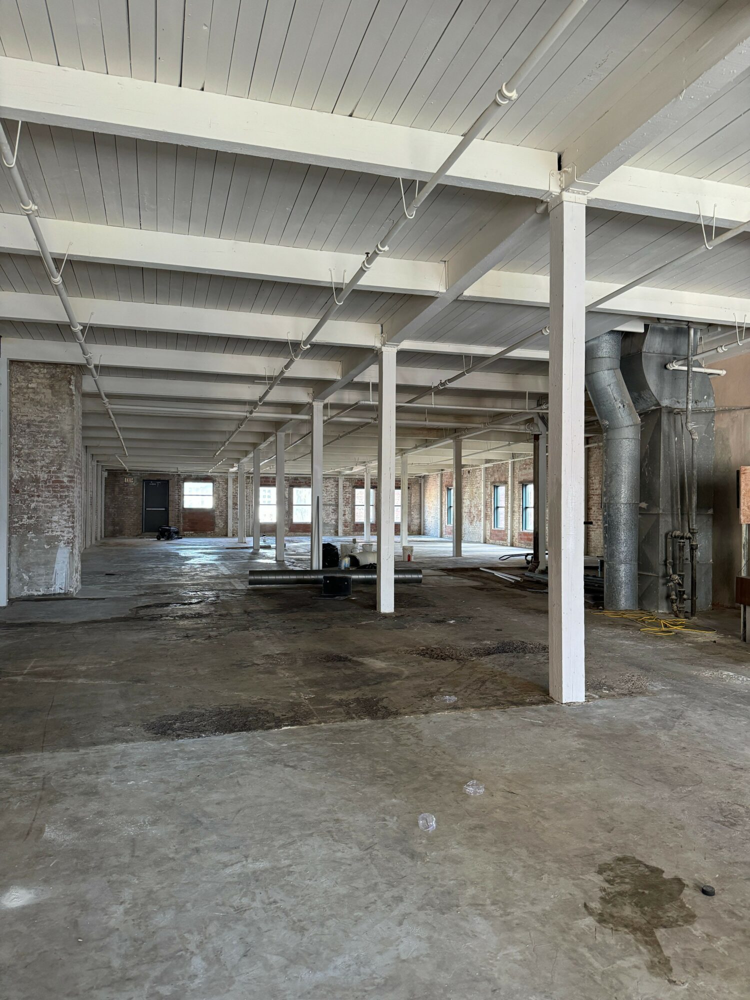 Empty industrial space with concrete floor, white ceiling, and large windows along the wall.