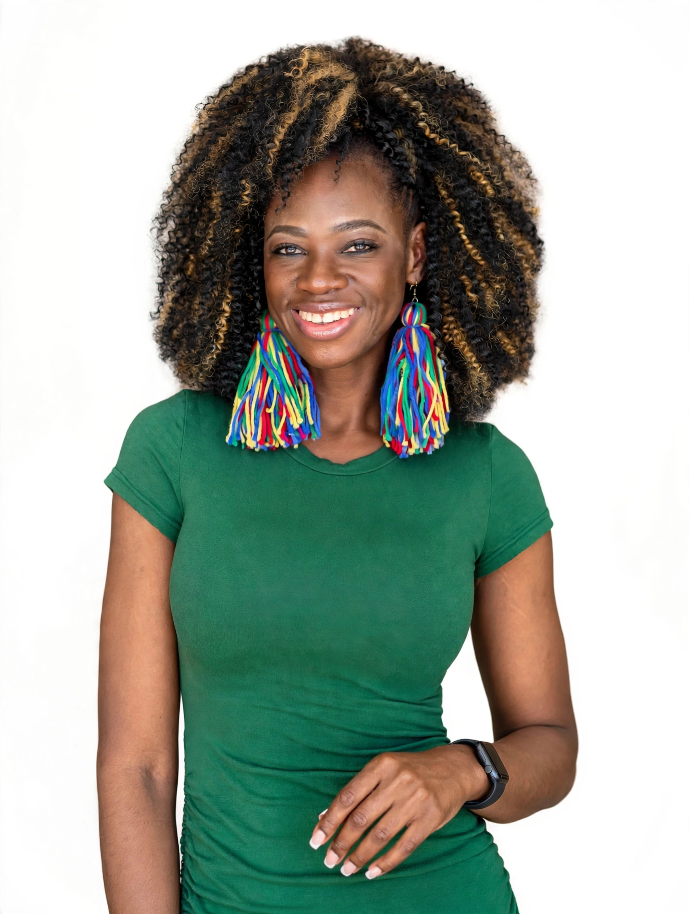 Smiling woman with curly hair wearing a green shirt and colorful earrings, standing against a white background.