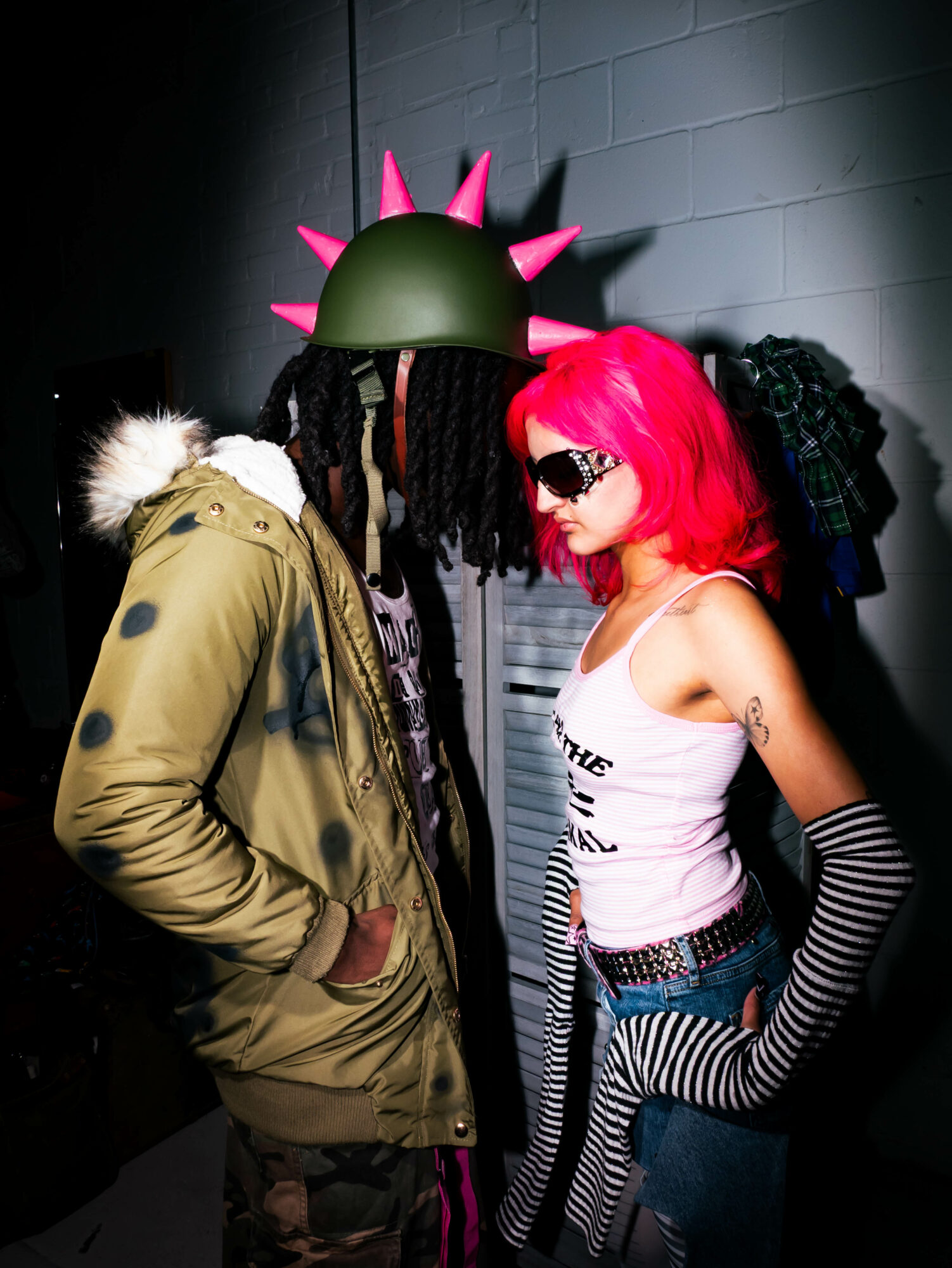 Two people with colorful hair and distinctive outfits face each other in a dark setting.