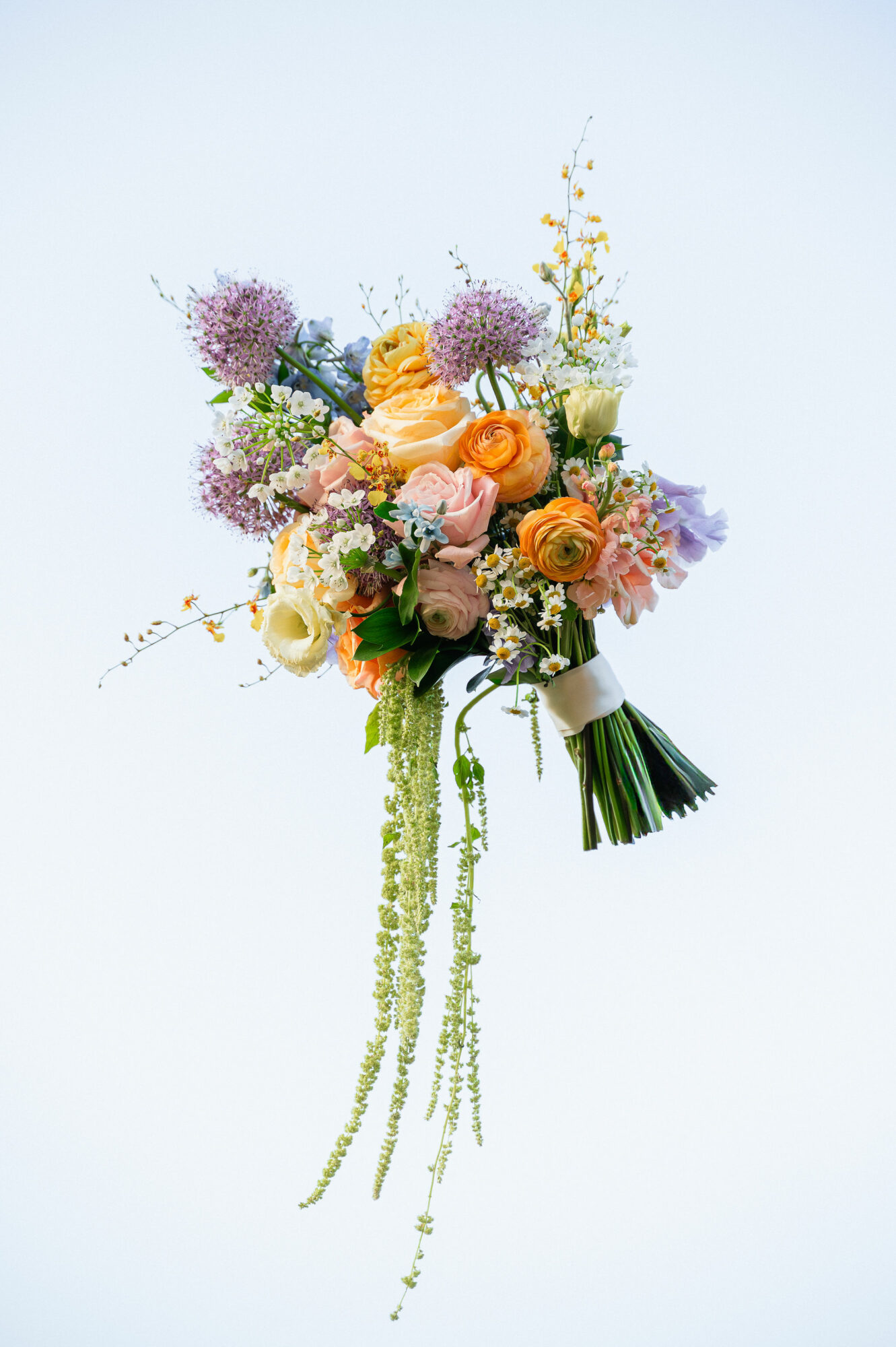 Colorful bouquet of roses, lavender, and greenery with long hanging flowers, against a light background.