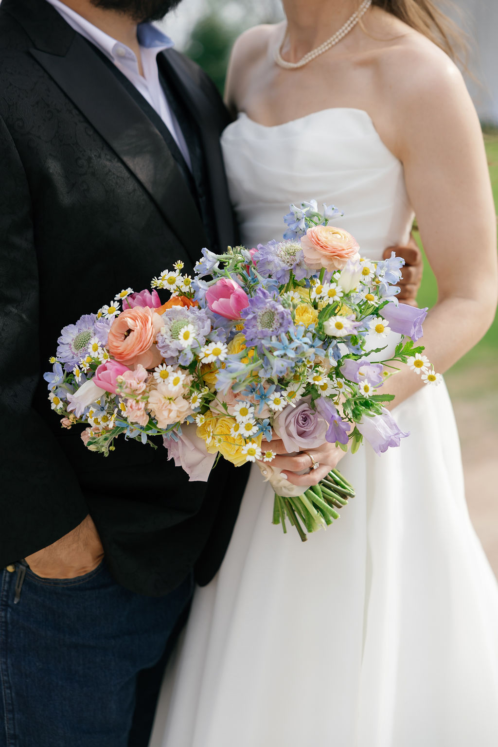 Bride and groom holding bouquets of colorful flowers, bride in white dress, groom in dark suit, close-up shot.
