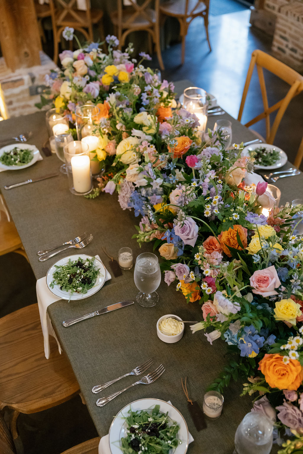 Table decorated with a colorful floral centerpiece, candles, and place settings with plates, glasses, and cutlery.