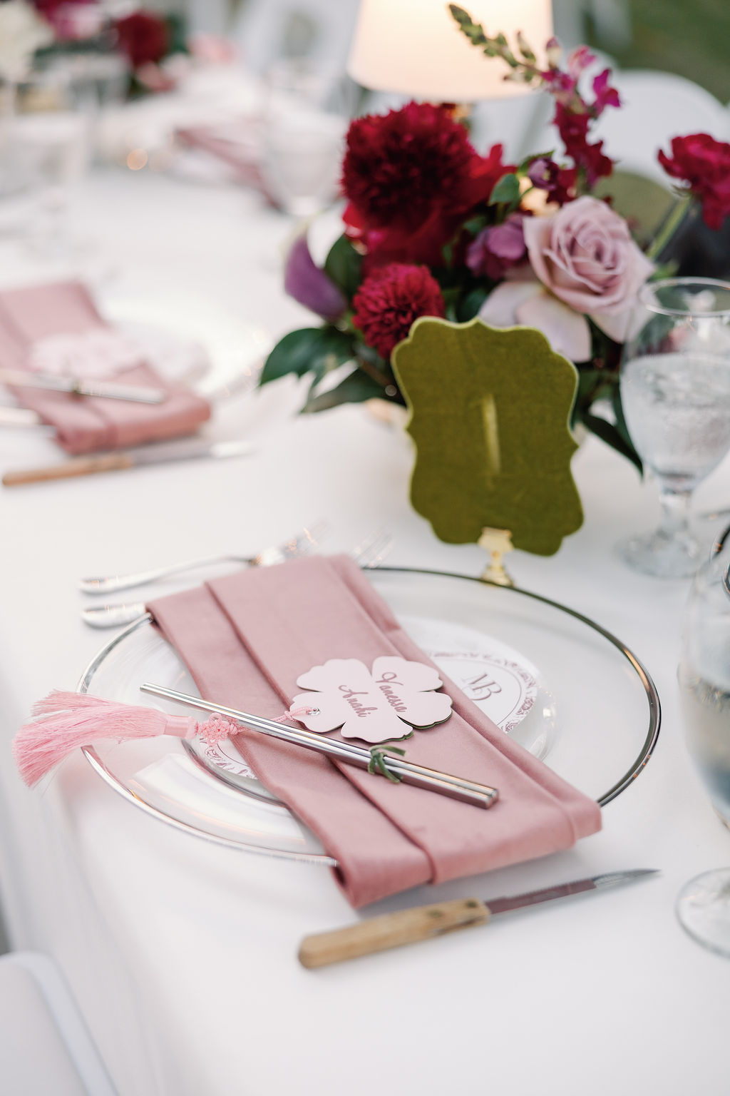 Table setting with pink napkin, silverware, and a floral centerpiece with pink and red flowers.