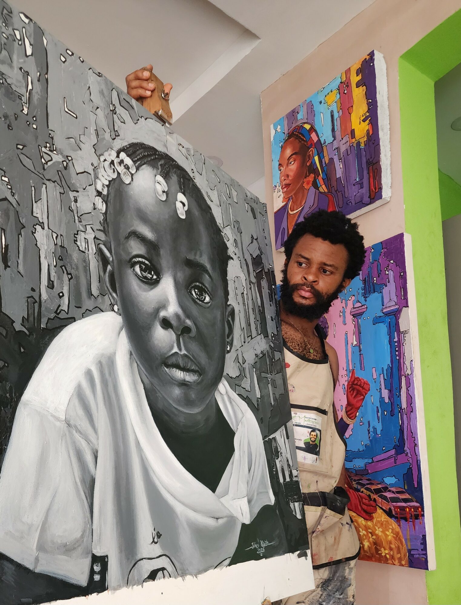 Man holding a large black-and-white portrait of a young girl with braided hair, surrounded by colorful paintings in an art gallery.
