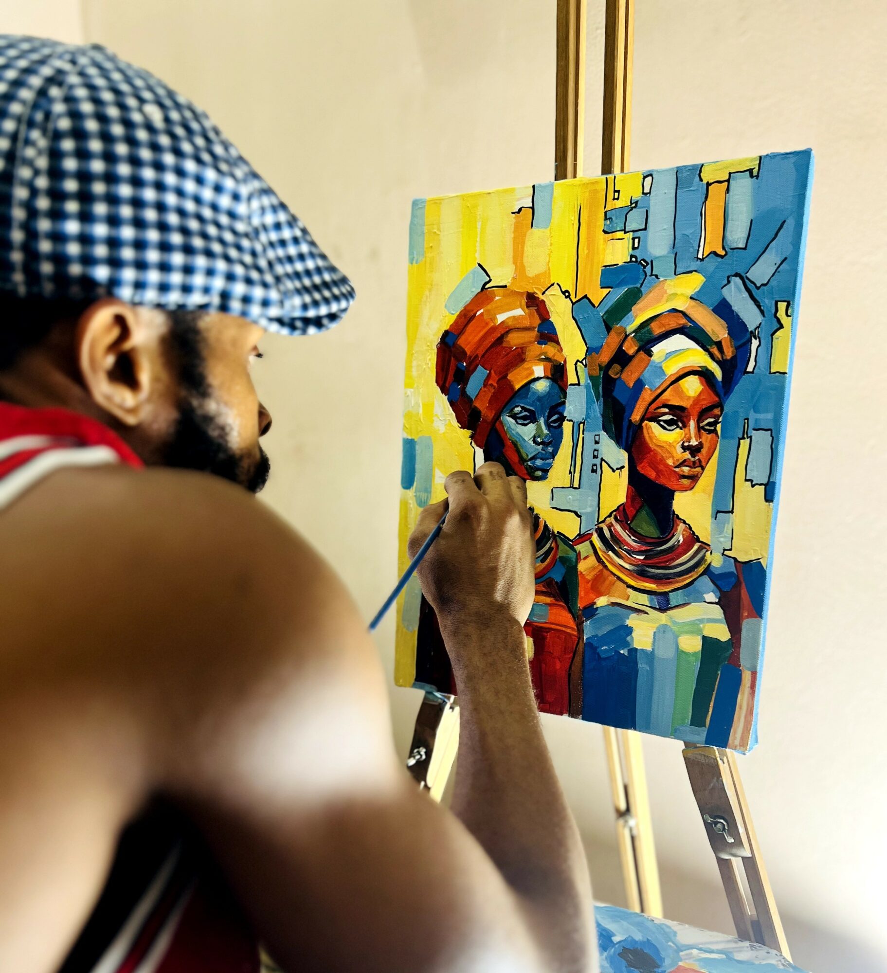 Artist painting a colorful portrait of two women on a canvas, wearing headwraps and jewelry, with a light background.
