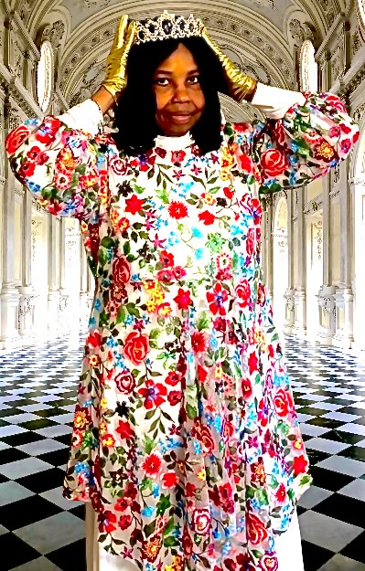 Woman wearing a floral dress and crown, standing in an ornate hall with checkered floor, holding crown with both hands.