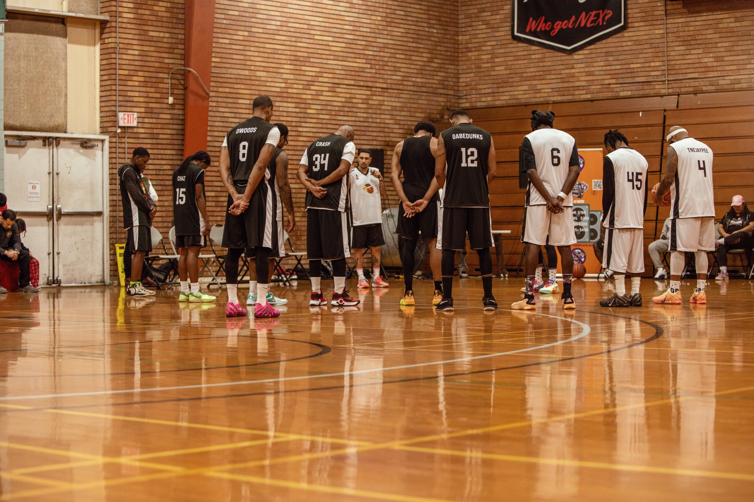 Basketball team standing on court, players in black and white uniforms, some with hands on hips, in a gymnasium.