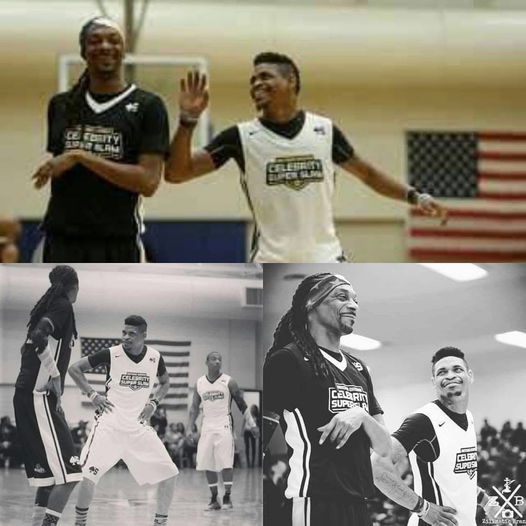 Two basketball players smiling and high-fiving indoors, with other players and an American flag in the background.