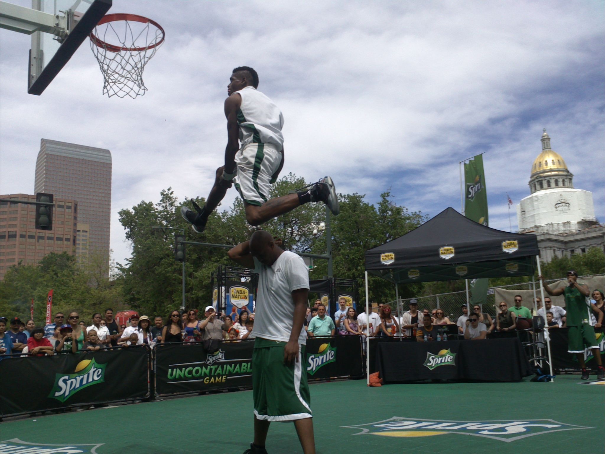 Basketball player dunking during game with crowd and cityscape in background.
