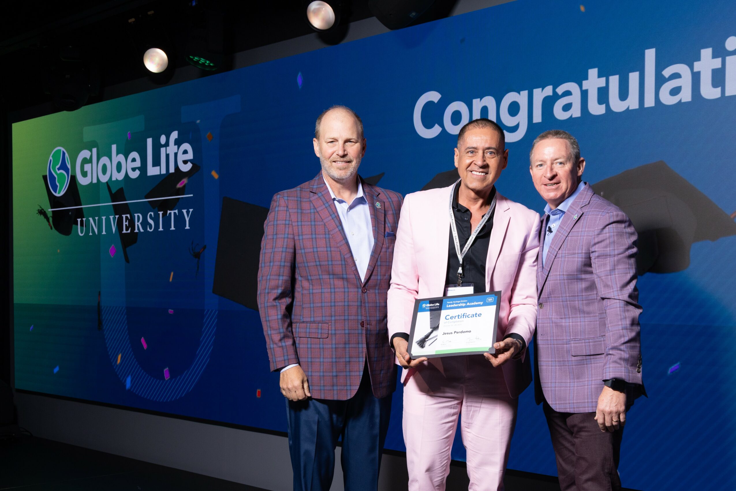 Three men standing in front of a blue backdrop with 'Globe Life University' and 'Congratulations' text, one holding a certificate.