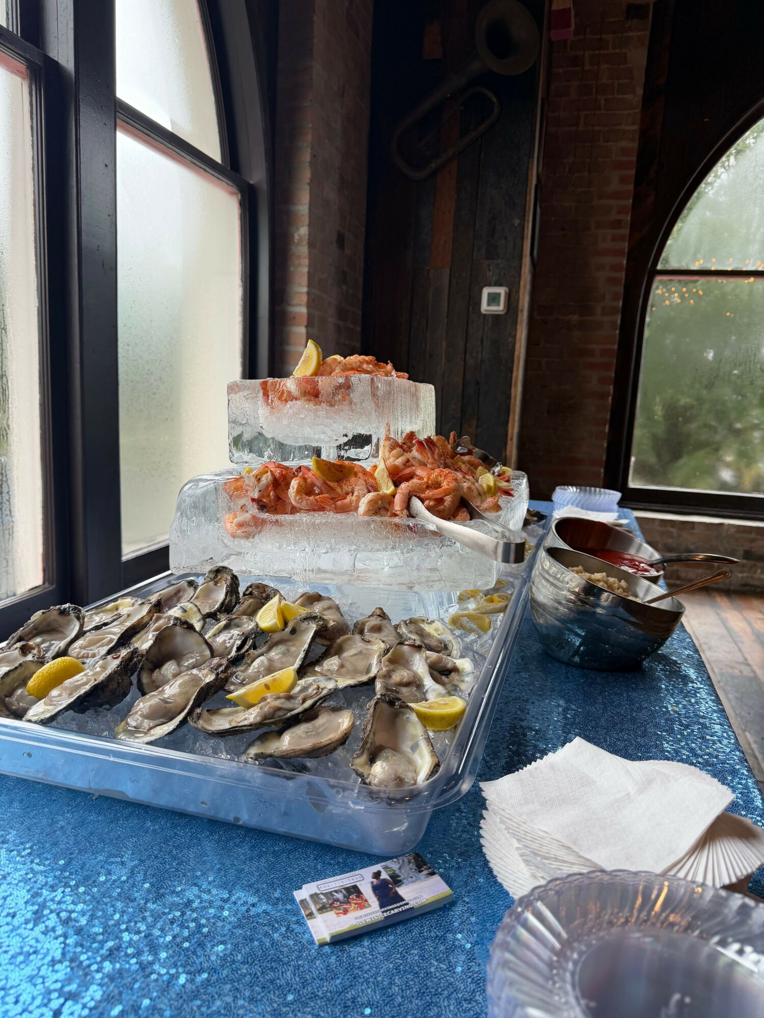A table with seafood, lemon wedges, and drinks, near a window with a view outside.