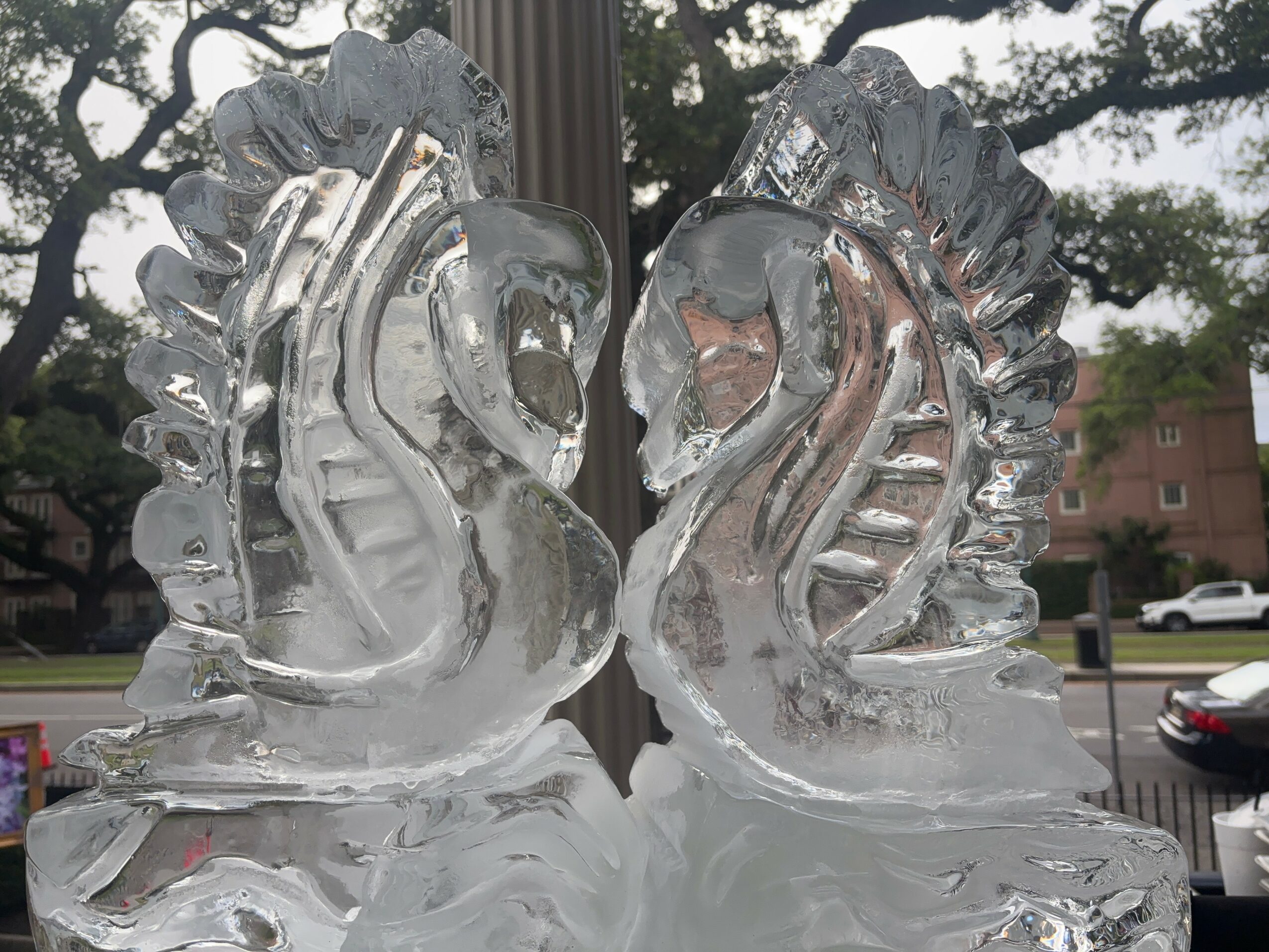 Two ice sculptures of swans facing each other with trees and buildings in the background.