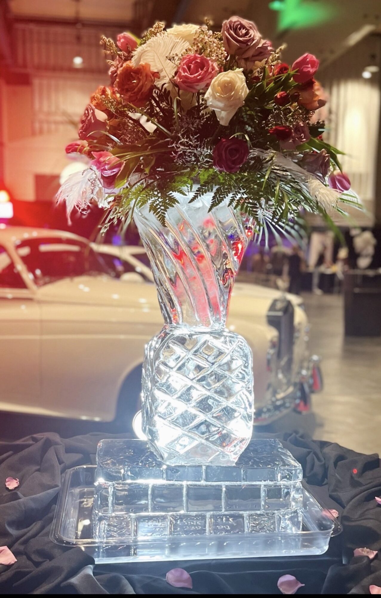 Elegant floral arrangement in a clear glass vase with roses and greenery, displayed on a glass base indoors.