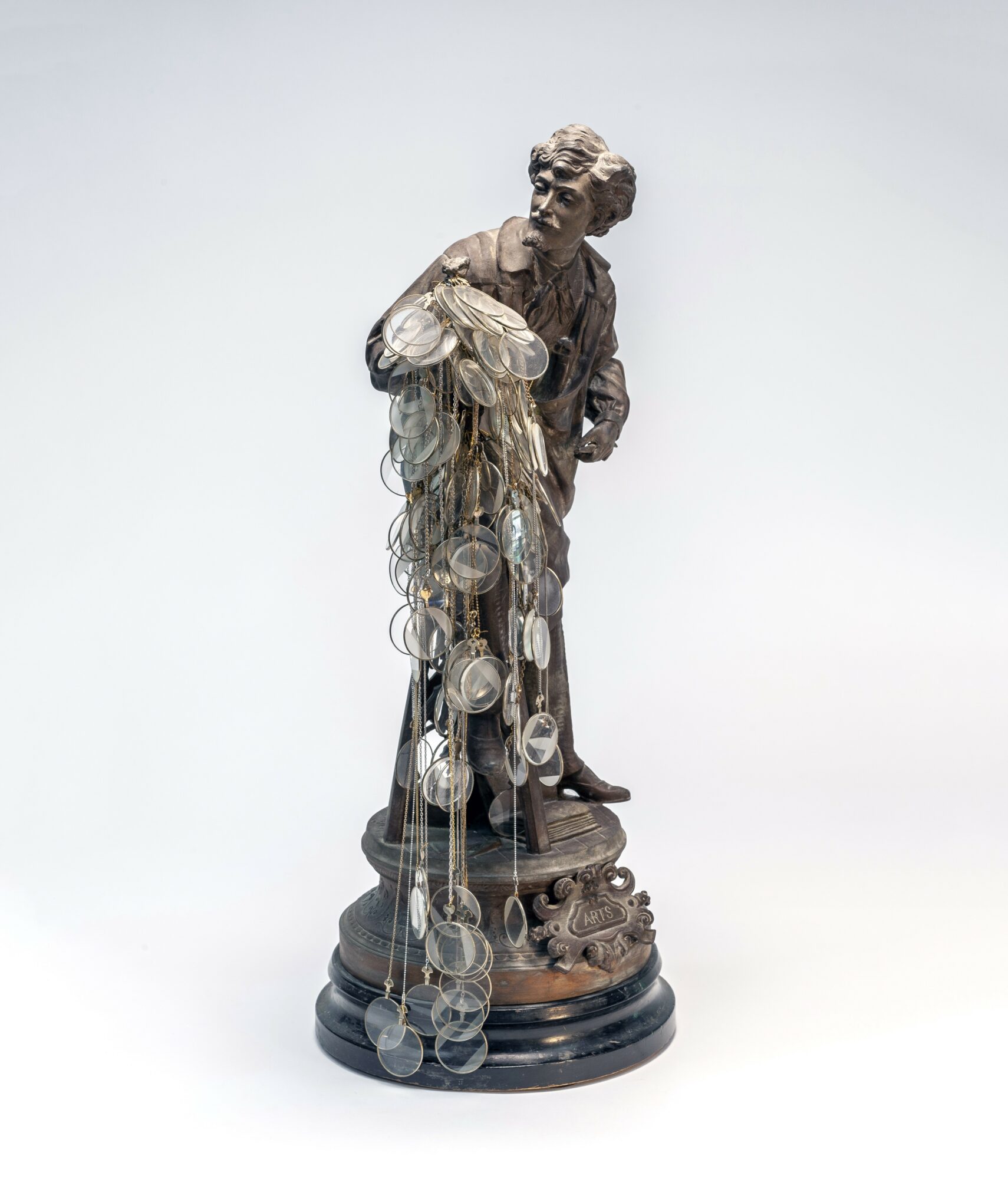 Statue of a person holding a bunch of coins, standing on a decorative base, with coins hanging from the figure's hand.