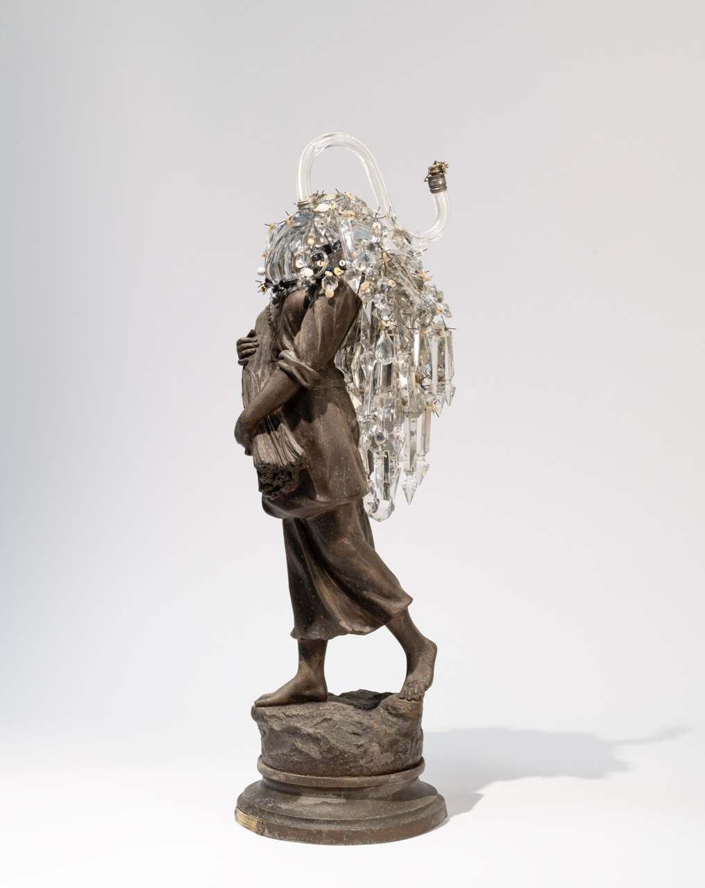 Sculpture of a person standing on a round base, holding a bouquet of flowers, with a decorative object on their back.