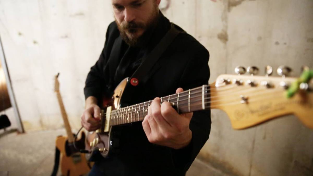 Person playing an electric guitar in a room with a concrete wall background.