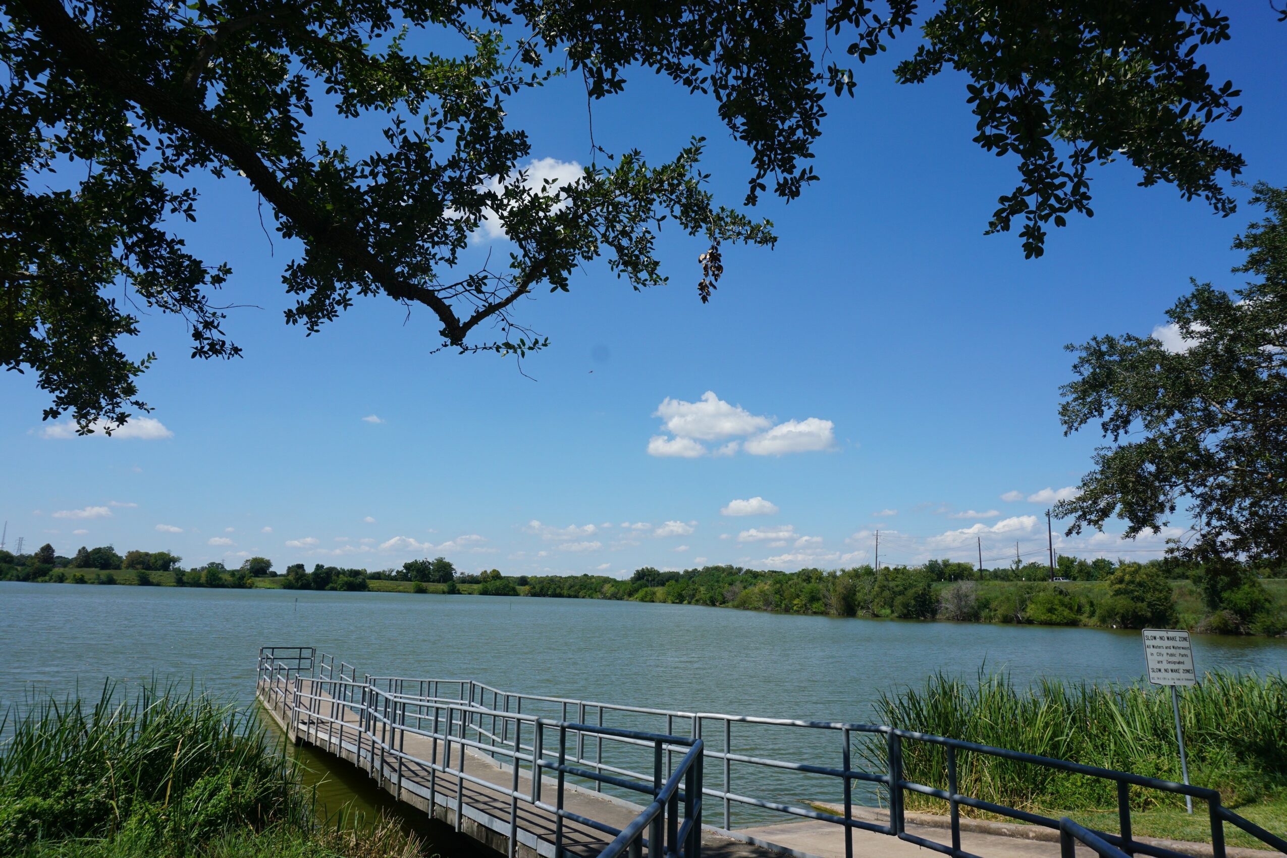 View of a lake with a dock, trees, and a blue sky with clouds.