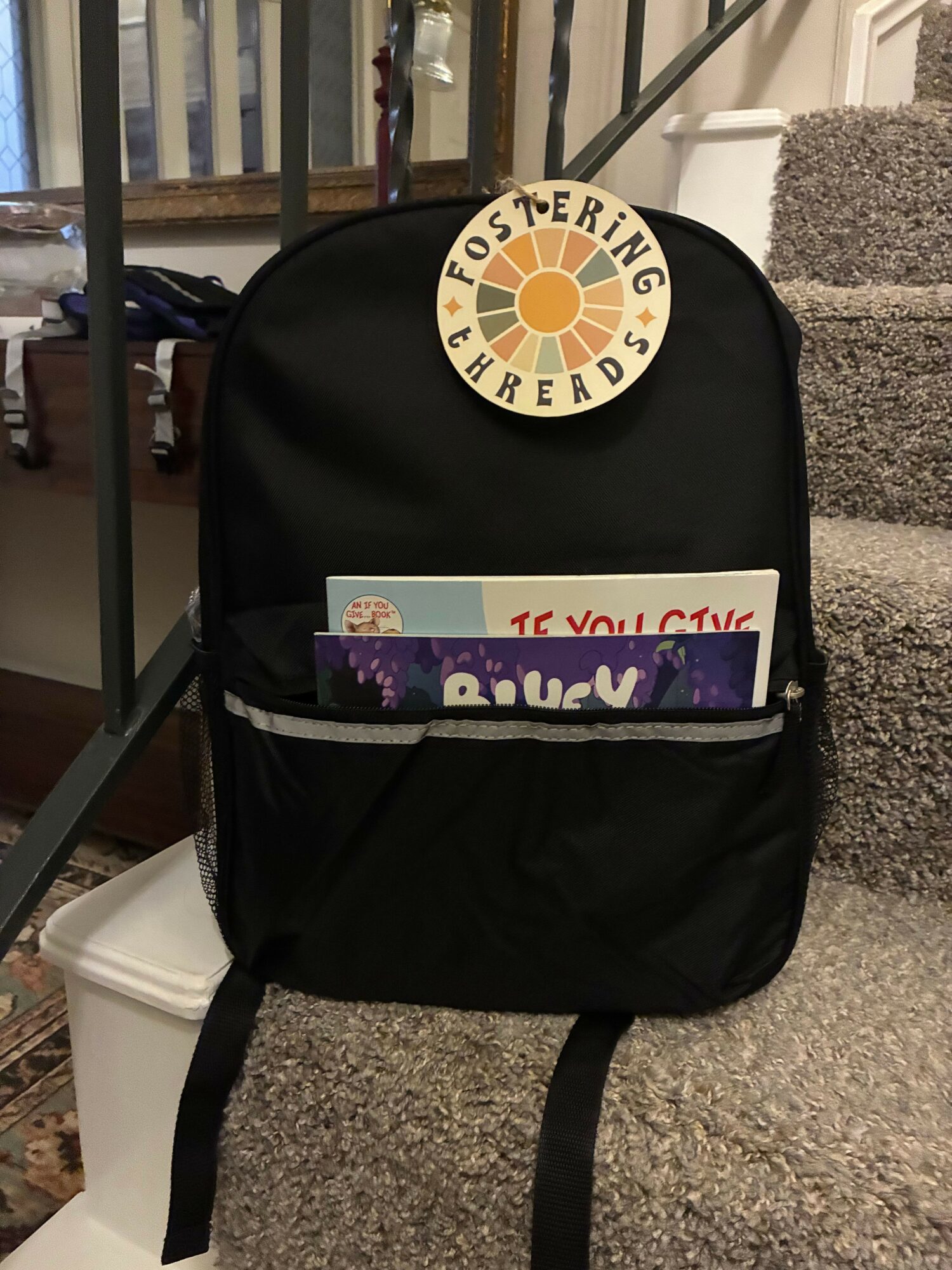 Black backpack with a circular patch and a sticker, placed on a metal railing, with a white object underneath.