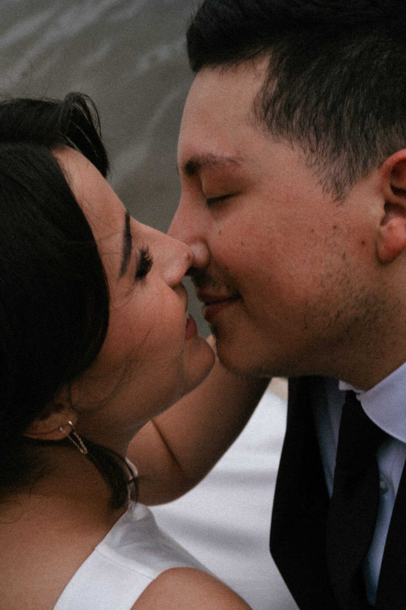 Two people face close with noses touching, eyes closed, smiling gently, in an intimate moment.