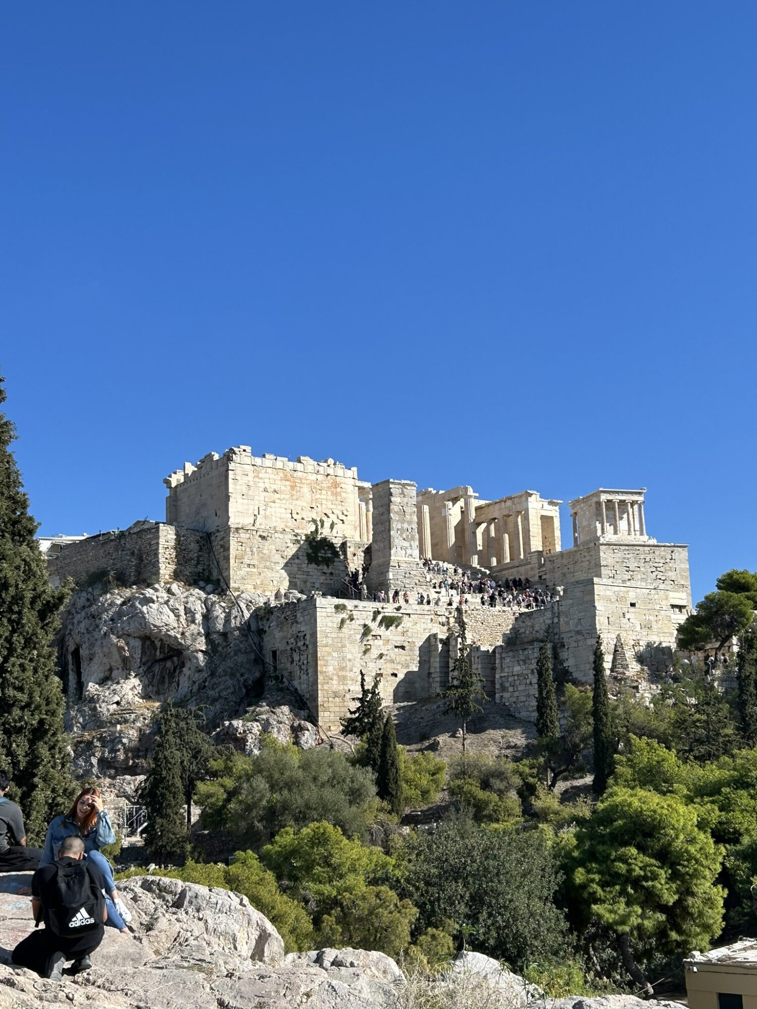 Ancient stone fortress on a hill with trees and greenery, under a clear blue sky.