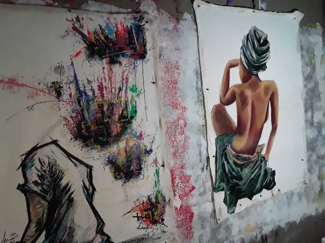 Two artworks on a wall: an abstract colorful painting and a realistic drawing of a seated, topless woman with a towel on her head.