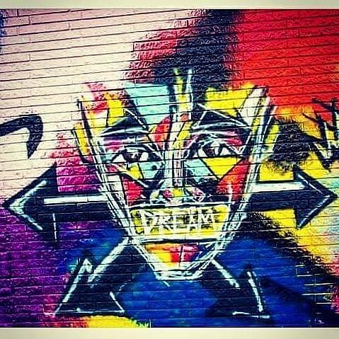 Colorful graffiti of a face with exaggerated features on a brick wall, with vibrant red, yellow, blue, and black colors.