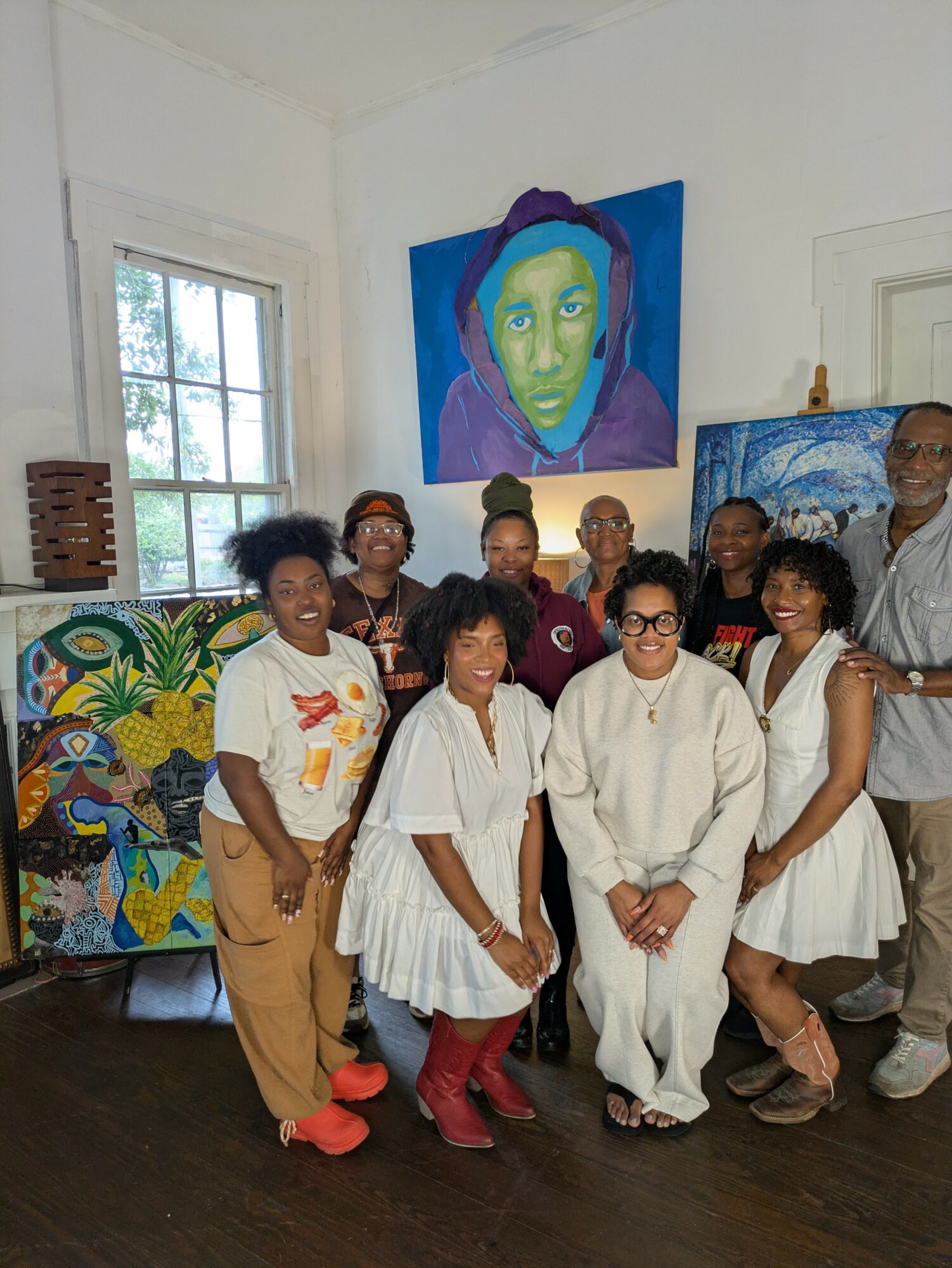 Group of eight people standing in an art gallery with colorful paintings on the wall, smiling at the camera.