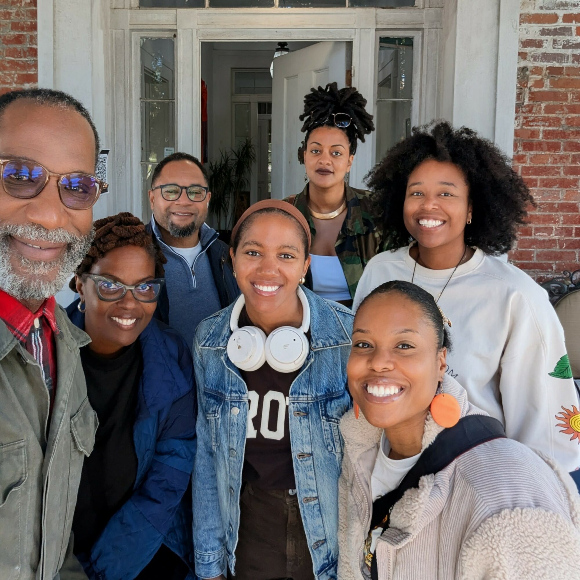 Group of seven diverse people smiling outside a building, posing for a photo.
