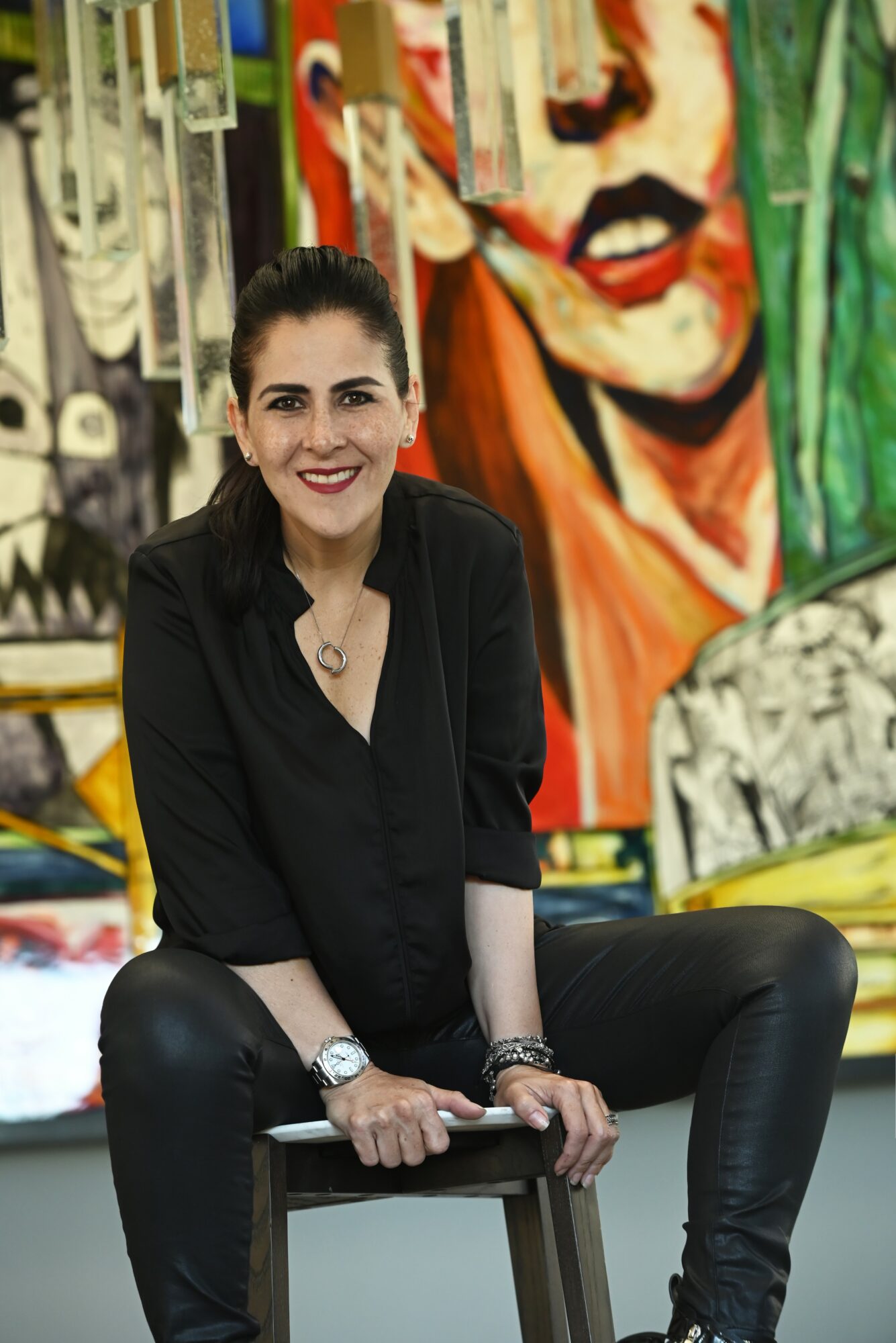 Woman sitting on a chair, smiling, with colorful abstract art in the background.