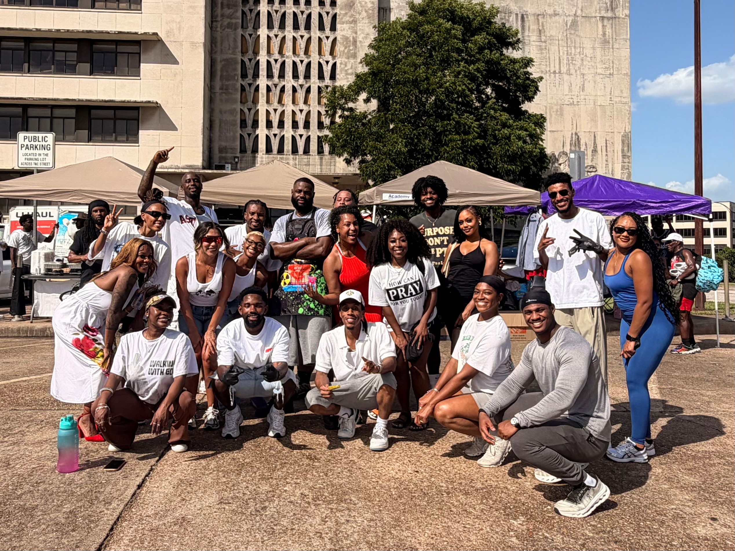Group of people outdoors in an urban area, some wearing white shirts, with tents and buildings in background.